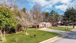 A residential street with houses, a well-maintained lawn, and a clear sky. - Midcentury Charm by the Pond (Winston-Salem)