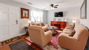 A living room with two beige armchairs, a small round table, a red cabinet, and a ceiling fan. - Midcentury Charm by the Pond (Winston-Salem)
