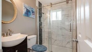 A bathroom with a glass shower enclosure, a white sink, and a blue toilet seat. - Downtown Winston's - 2 BR - Queens - Pad 2 (Winston-Salem)