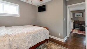 A bedroom with a bed, a ceiling fan, a television on the wall, and a view of the hallway. - Downtown Winston's - 2 BR - Queens - Pad 2 (Winston-Salem)