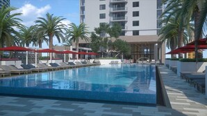 A swimming pool with lounge chairs and umbrellas, surrounded by palm trees and a modern building.