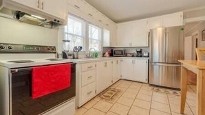 Una cocina con armarios blancos, una toalla roja sobre el horno, un microondas y un refrigerador.