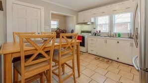 Una cocina compacta con gabinetes blancos, una mesa de comedor con sillas de madera y un refrigerador.