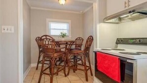 Una cocina con una mesa de comedor y cuatro sillas, estufa y ventana con persianas.