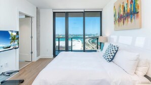 A modern hotel room with a large bed, a TV, and a balcony with a city view.