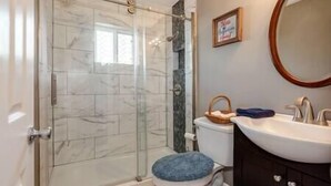 Ein Badezimmer mit Duschkabine aus Glas, Toilette und Waschbecken mit Spiegel.