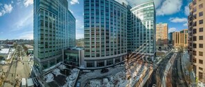 A modern multi-story building with a curved facade, large windows, and a parking area with snow. - Near Hospitals 2 BR | Pet Friendly w Dog Run (White Plains)