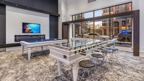 A modern indoor pool table with stools, a large TV screen, and a view of the outside through large windows.