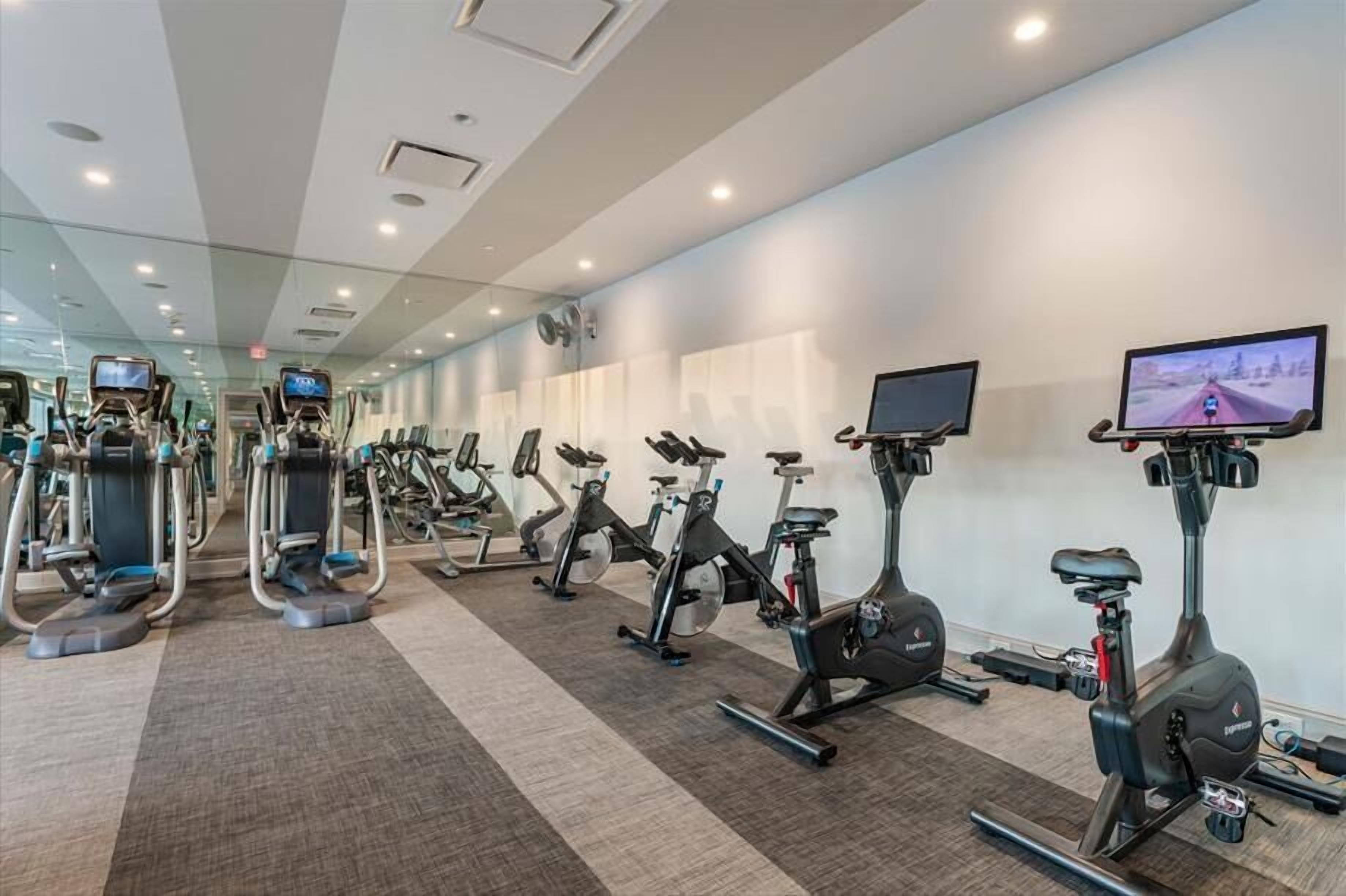 Une salle de sport équipée de divers appareils d’exercice, notamment des tapis de course et des vélos d’appartement, disposés en rangées.