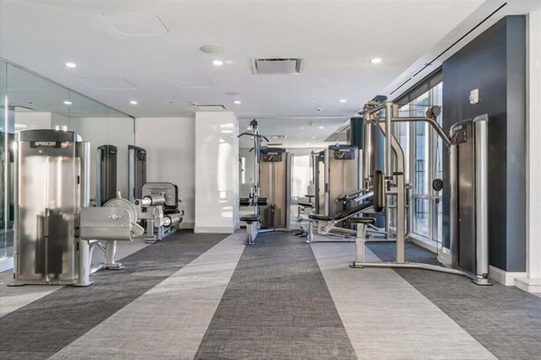 A modern gym with various exercise machines, a mirrored wall, and a carpeted floor.