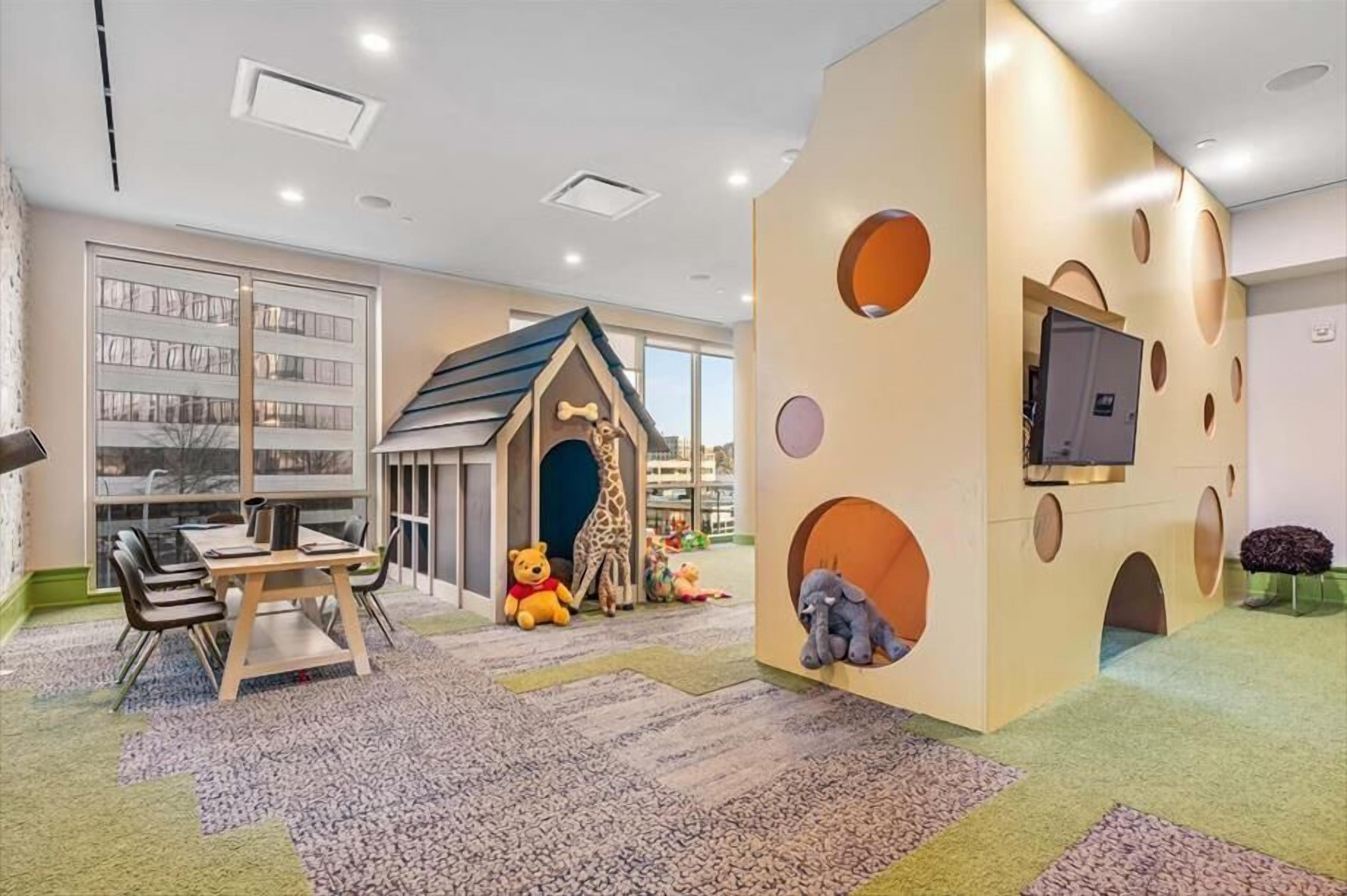 A children's play area with a giraffe-themed playhouse, a table with chairs, and a television mounted on a wall.