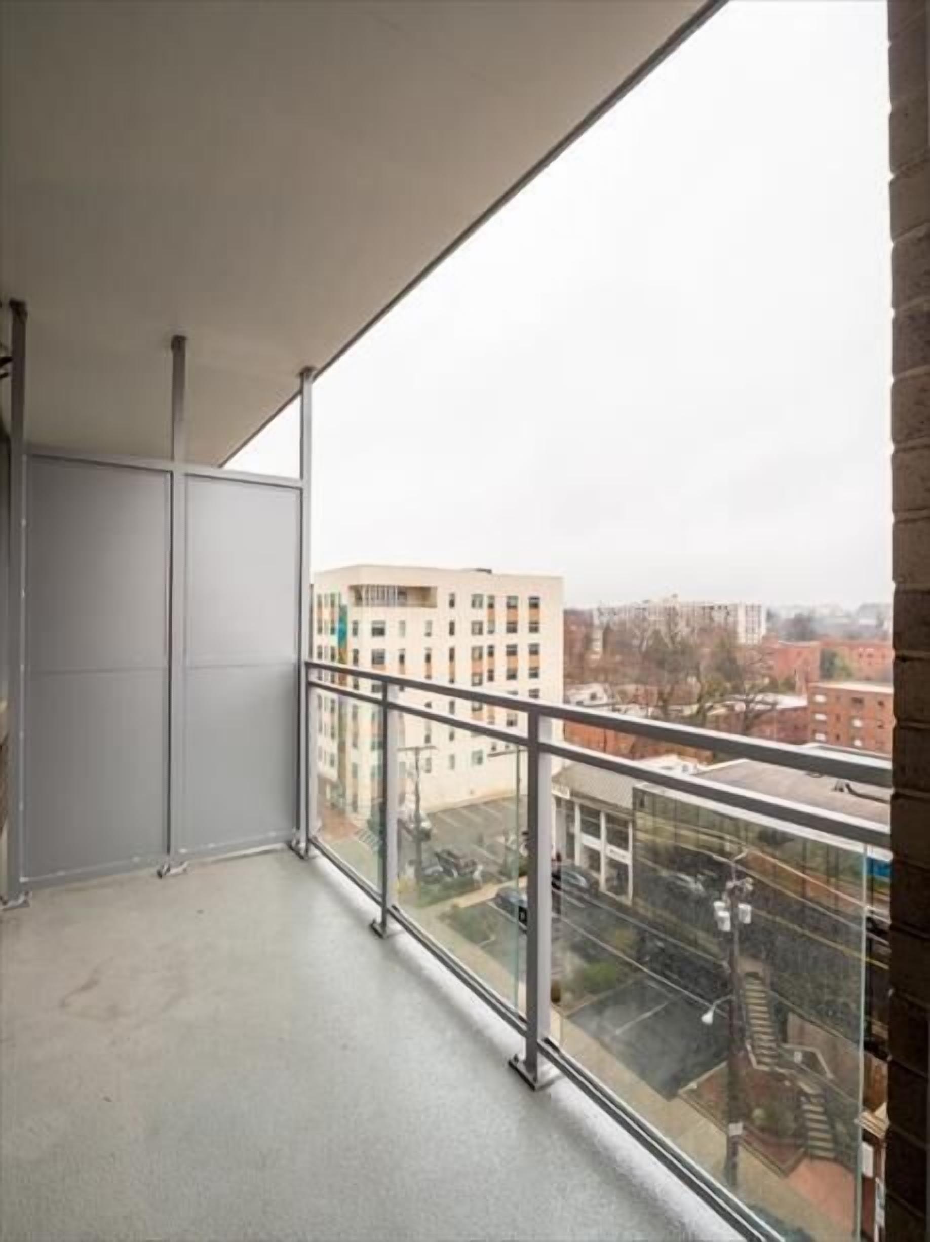 Un balcon doté d’une balustrade en verre donnant sur un paysage urbain.