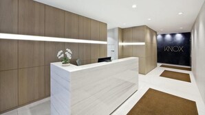 Un espace d’accueil moderne, doté d’un comptoir de réception de couleur claire, de murs recouverts de panneaux en bois et d’un mur noir sur lequel est inscrit le mot « INOX ».