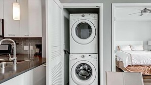 A compact hotel room with a washer and dryer, a kitchenette, a bed, and a bedside table.