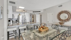 A modern kitchen with white cabinets, a stainless steel refrigerator, and a dining area with a glass table and metal chairs. - 3 Bedrooms and 3 baths : Beach Facing Condo (Orange Beach)