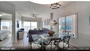 A spacious room with a glass dining table, a sofa, and a ceiling fan. There are three beds and three bathrooms. The room has large windows and a balcony. - 3 Bedrooms and 3 baths : Beach Facing Condo (Orange Beach)