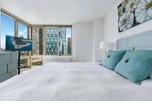 Quarto com uma cama grande, vista para a cidade pela janela e um quadro na parede.