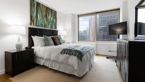A modern bedroom with a large bed, a nightstand, a dresser, a TV, and a city view. - Columbus Cirle 1 BR city | Work Space | Midtown (New York)