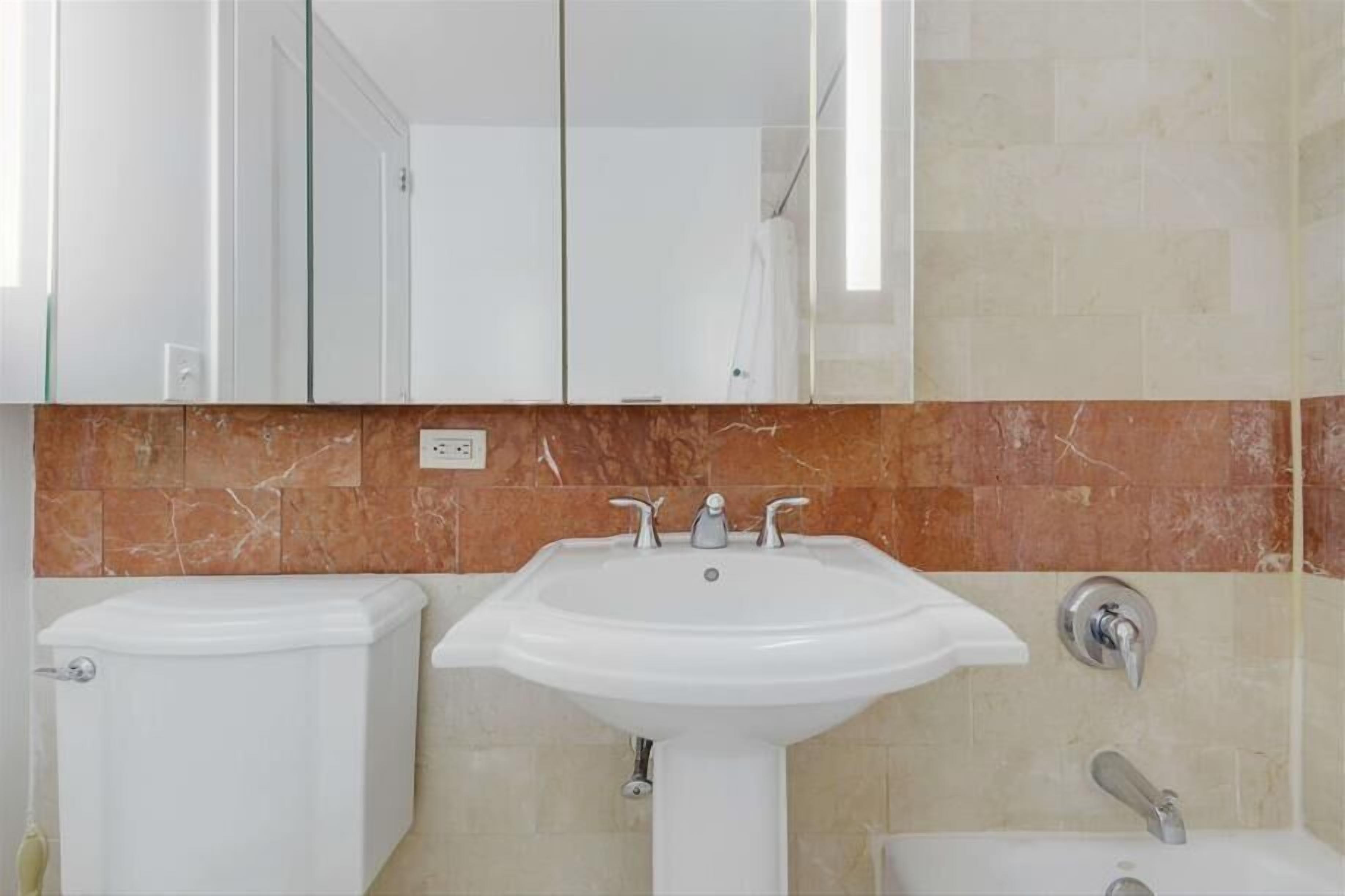 Un baño con un lavamanos blanco, un inodoro y un espejo sobre el lavamanos.