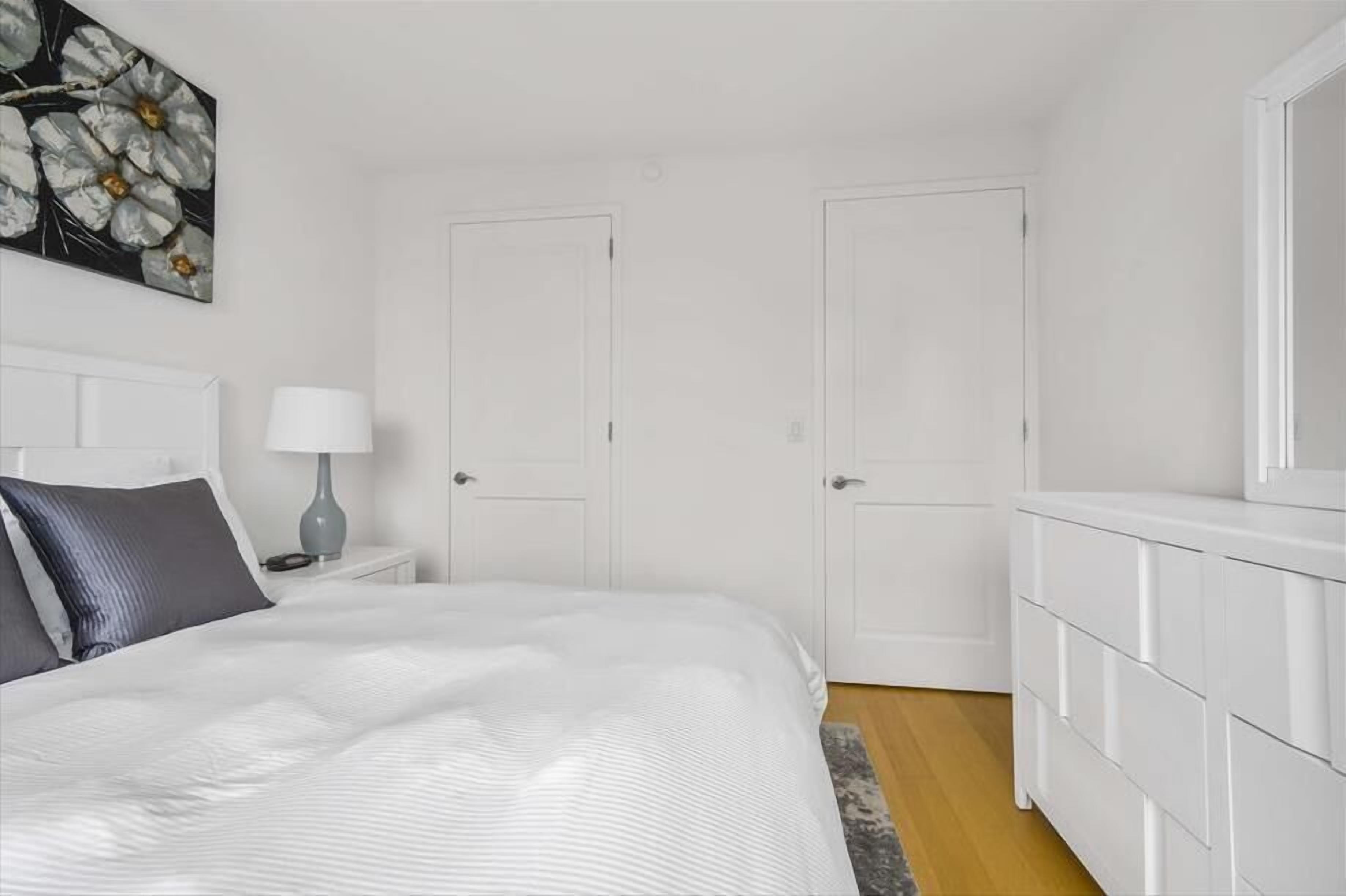 A bedroom with a bed, a nightstand, a dresser, and two doors.