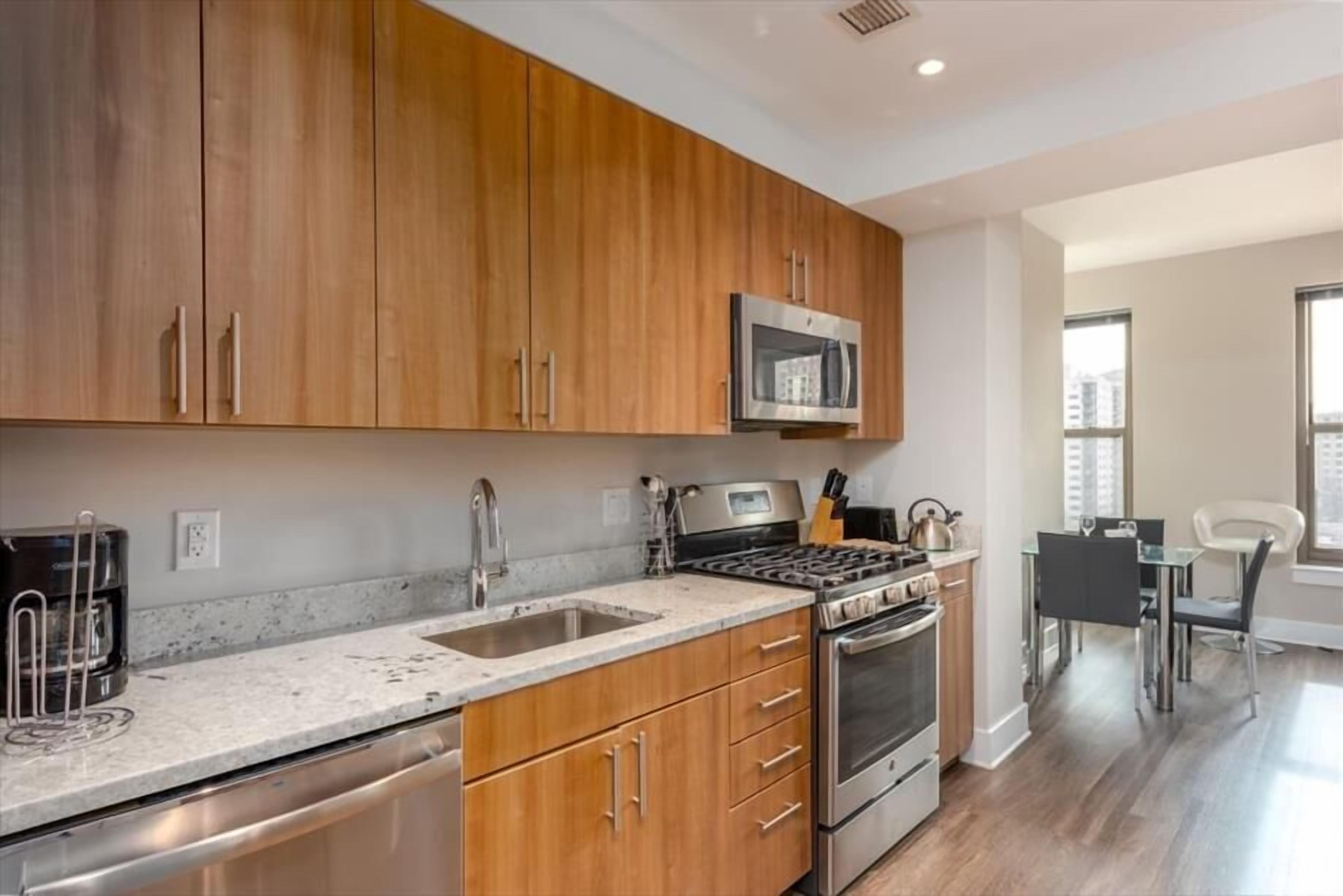 A modern kitchen with wooden cabinets, stainless steel appliances, and a dining area with a glass table and chairs.