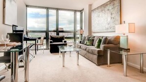A modern living room with a glass coffee table, a sofa, and a dining area with a piano. - 10 min drive to Capitol 2 BR | Business Center (Arlington)