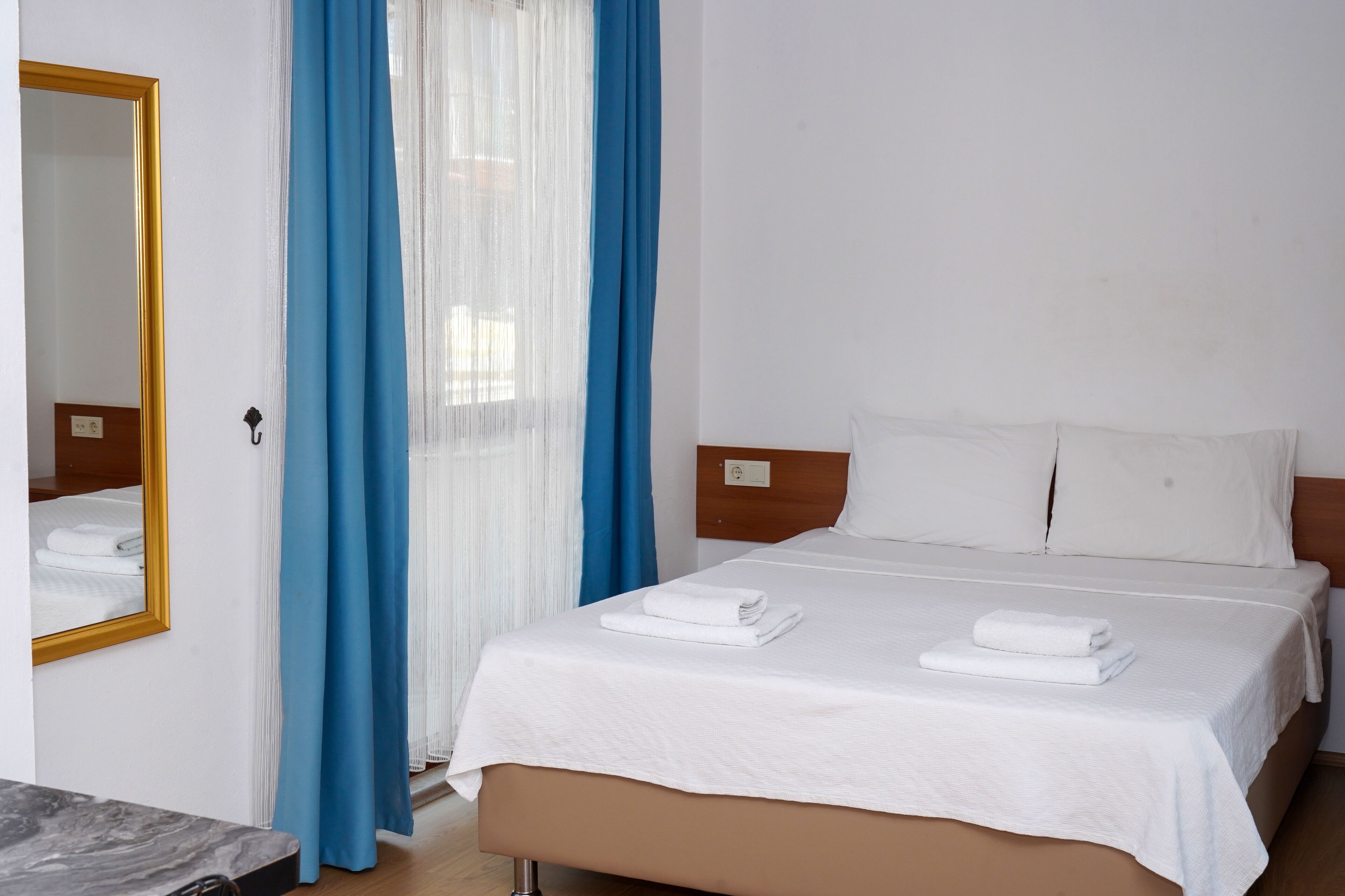 A hotel room with a bed, a mirror, and a window with blue curtains.