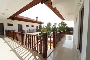 A spacious balcony with a wooden railing, a tiled floor, and a view of a building with a tiled roof and greenery in the background. - Akyaka Nehir Butik Otel (Ula)