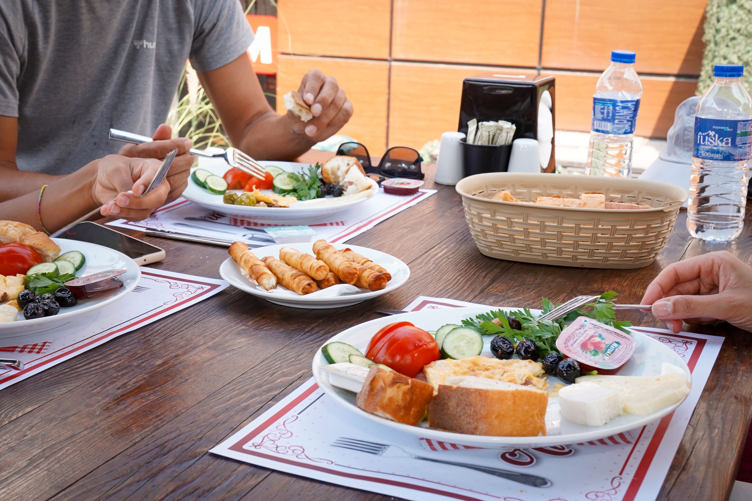 A wooden table with plates of food, a basket, and a water bottle.