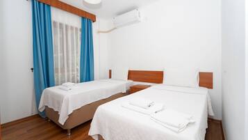 A hotel room with two single beds, a wooden headboard, a window with blue curtains, and an air conditioning unit.