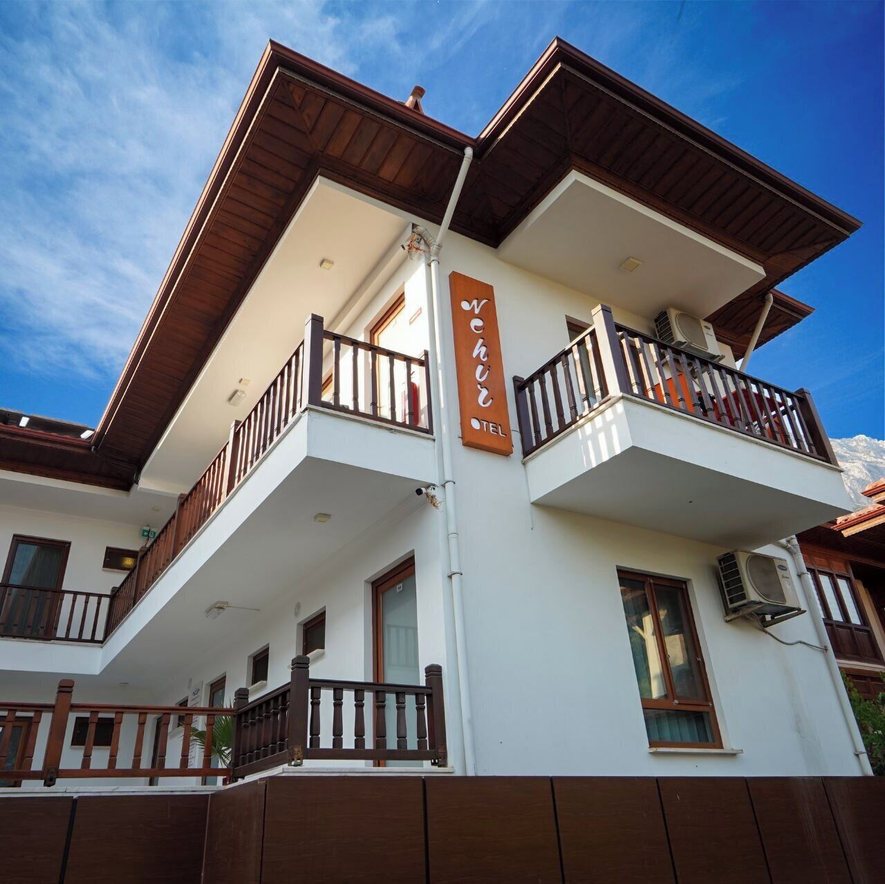 Un hotel de varios pisos con balcones, una señal que indica que es un hotel, y un cielo despejado.