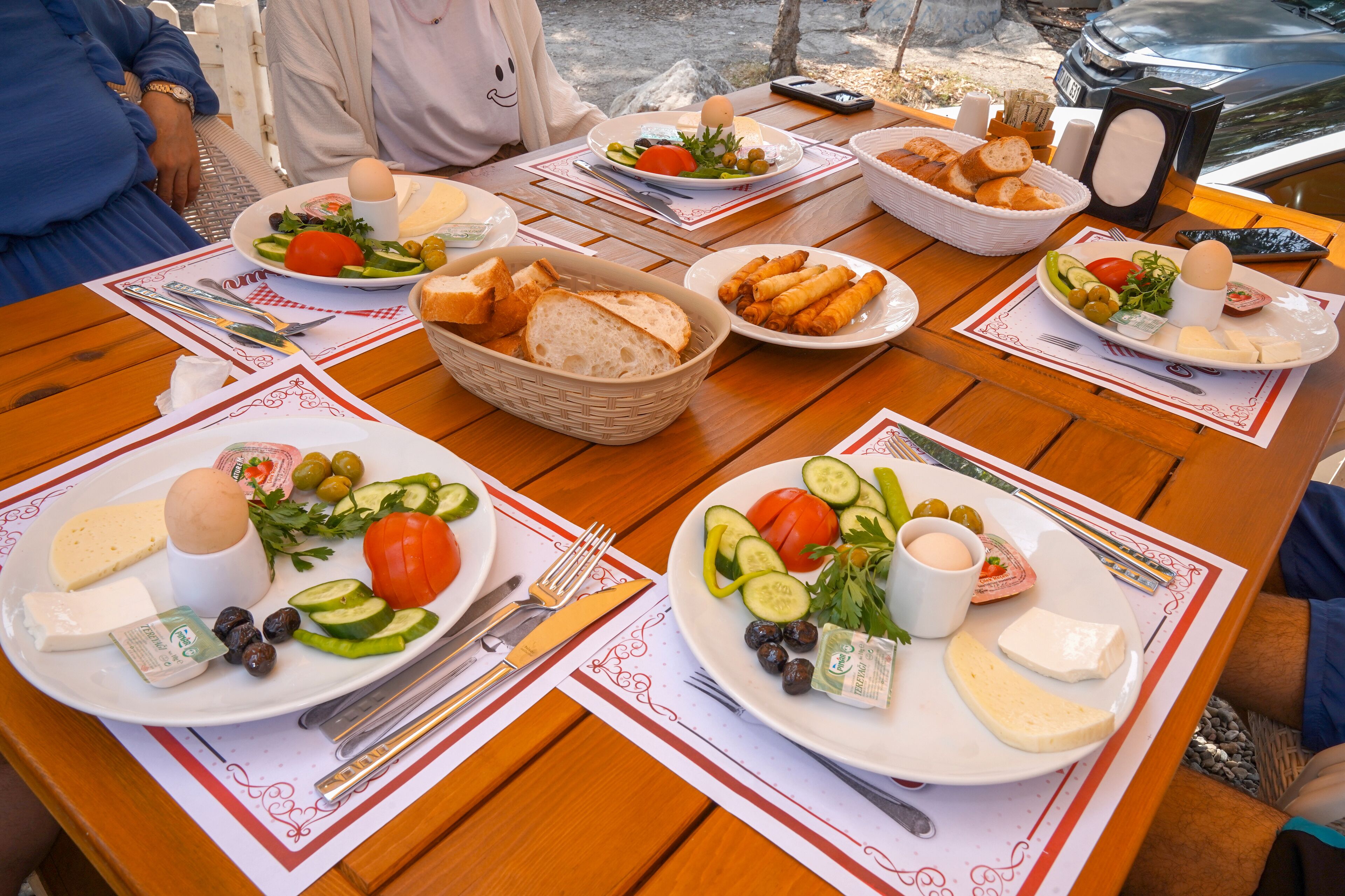 A table set with plates of food, including cheese, olives, and vegetables, and a basket of bread.
