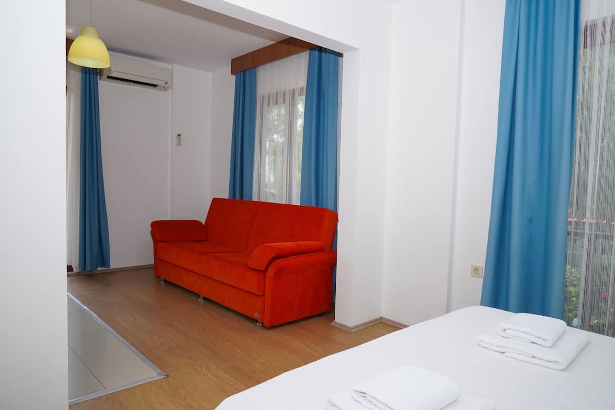 Um quarto com uma cama, um sofá vermelho e uma janela com cortinas azuis.