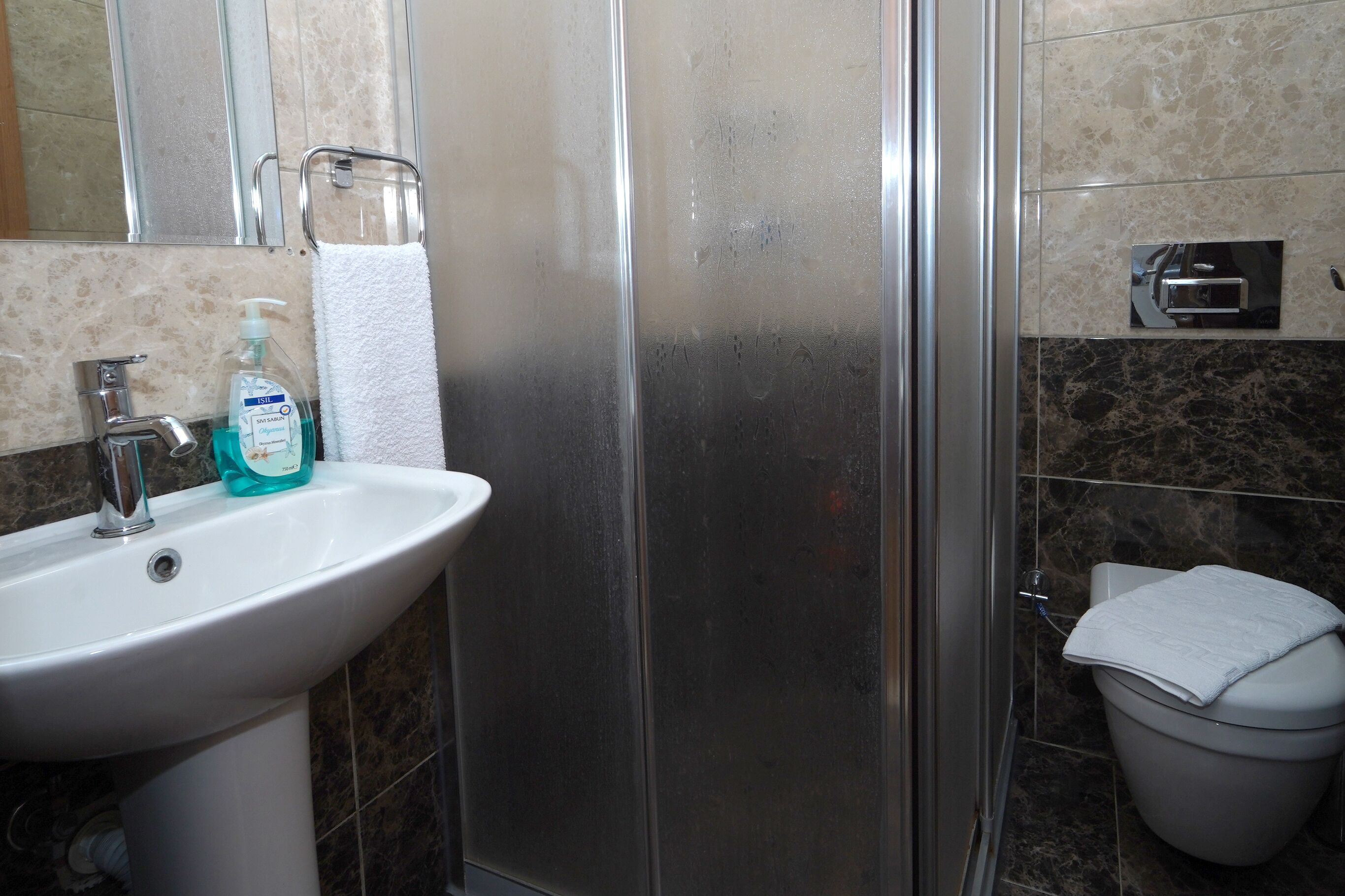 A bathroom with a white sink, a glass shower enclosure, and a toilet with a towel on top.