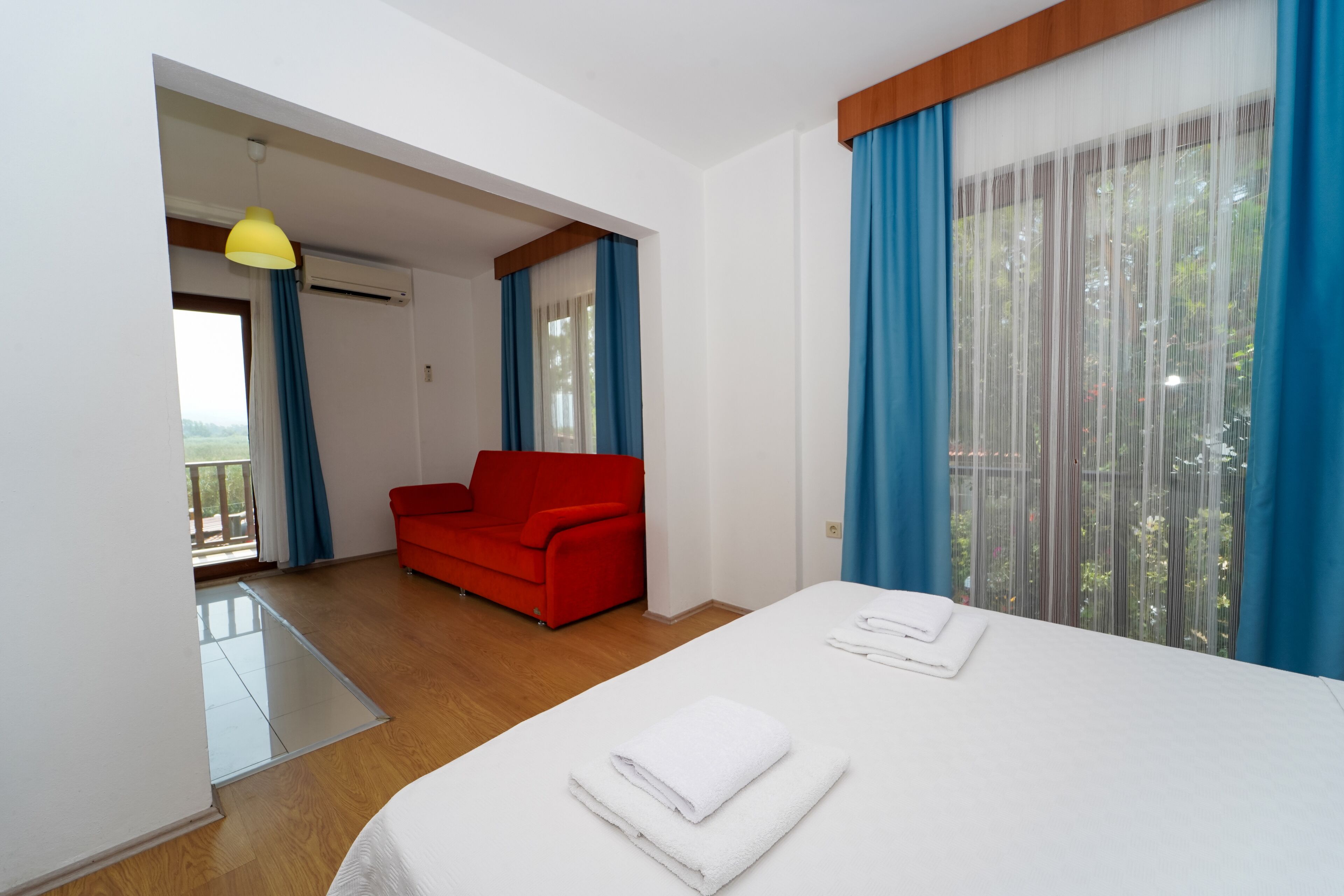 Een hotelkamer met een bed, een rode bank en een balkon met blauwe gordijnen.