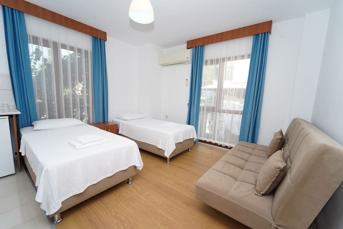 Quarto de hotel com duas camas, um sofá, uma mesinha e um ar condicionado.