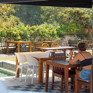 An outdoor patio area with wooden tables and chairs, a small pool, and lush greenery in the background. - Akyaka Nehir Butik Otel (Ula)