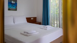 A neatly made bed with white linens and towels, a wooden headboard, and a painting of a sailboat on the wall. - Akyaka Nehir Butik Otel (Ula)