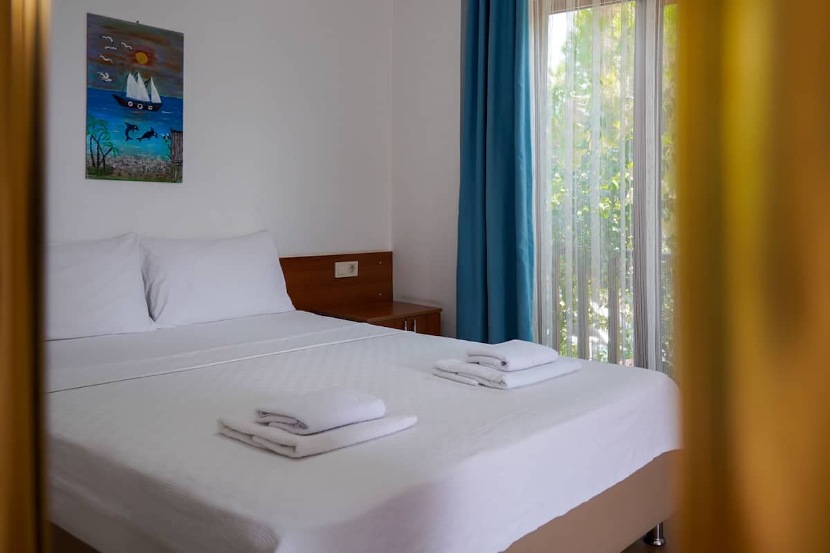 Cama bem arrumada com lençóis e toalhas brancos, cabeceira de madeira e um quadro de um veleiro na parede.