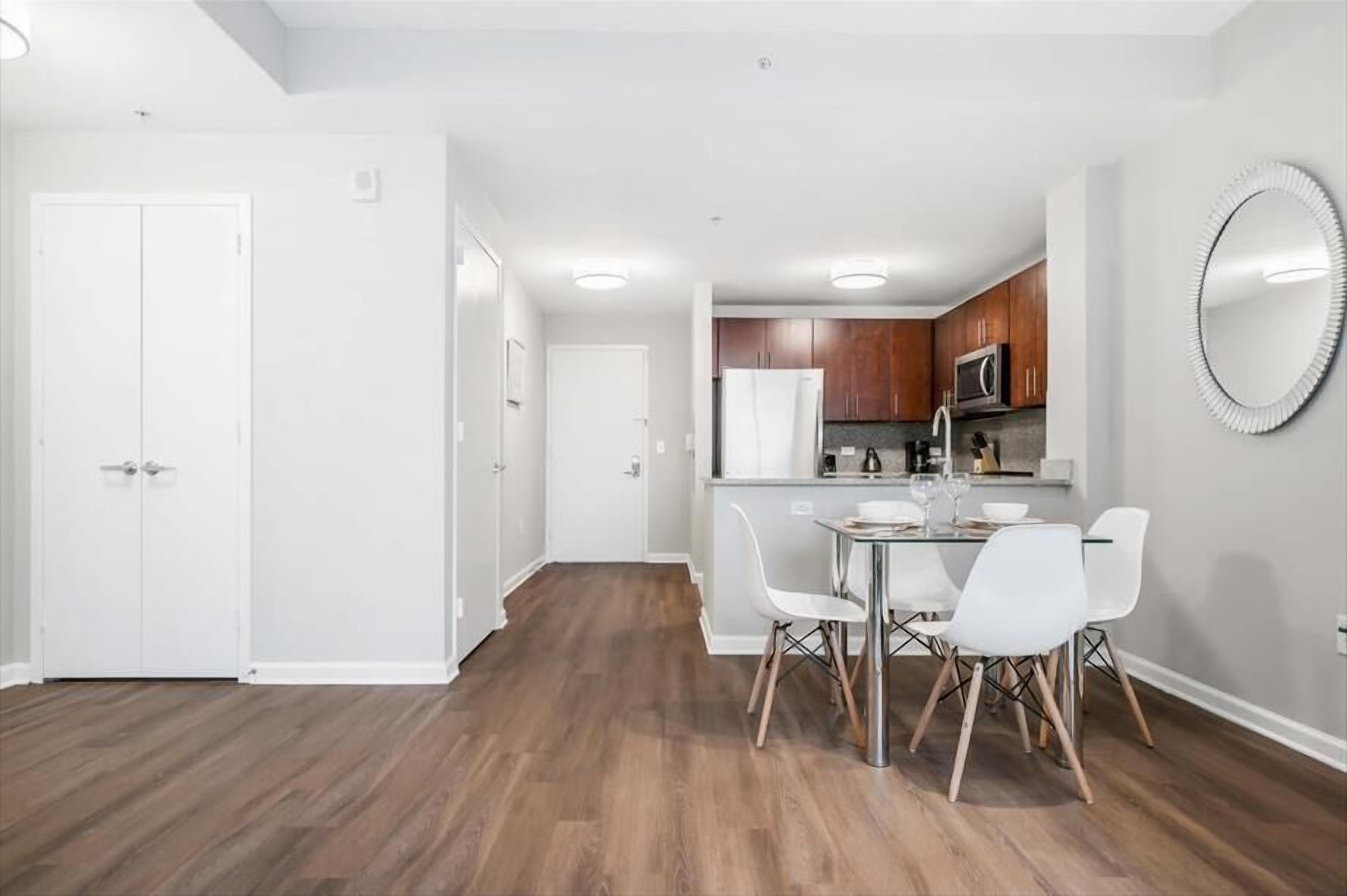 A modern apartment with a dining area, kitchen, and a large mirror.