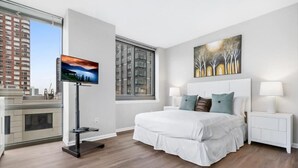 Habitación de hotel moderna con una cama grande, televisión de pantalla plana, un cuadro en la pared y vistas a la ciudad desde la ventana.