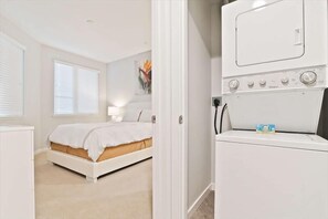 Une chambre à coucher avec un lit, un lave-linge et une fenêtre avec des stores.
