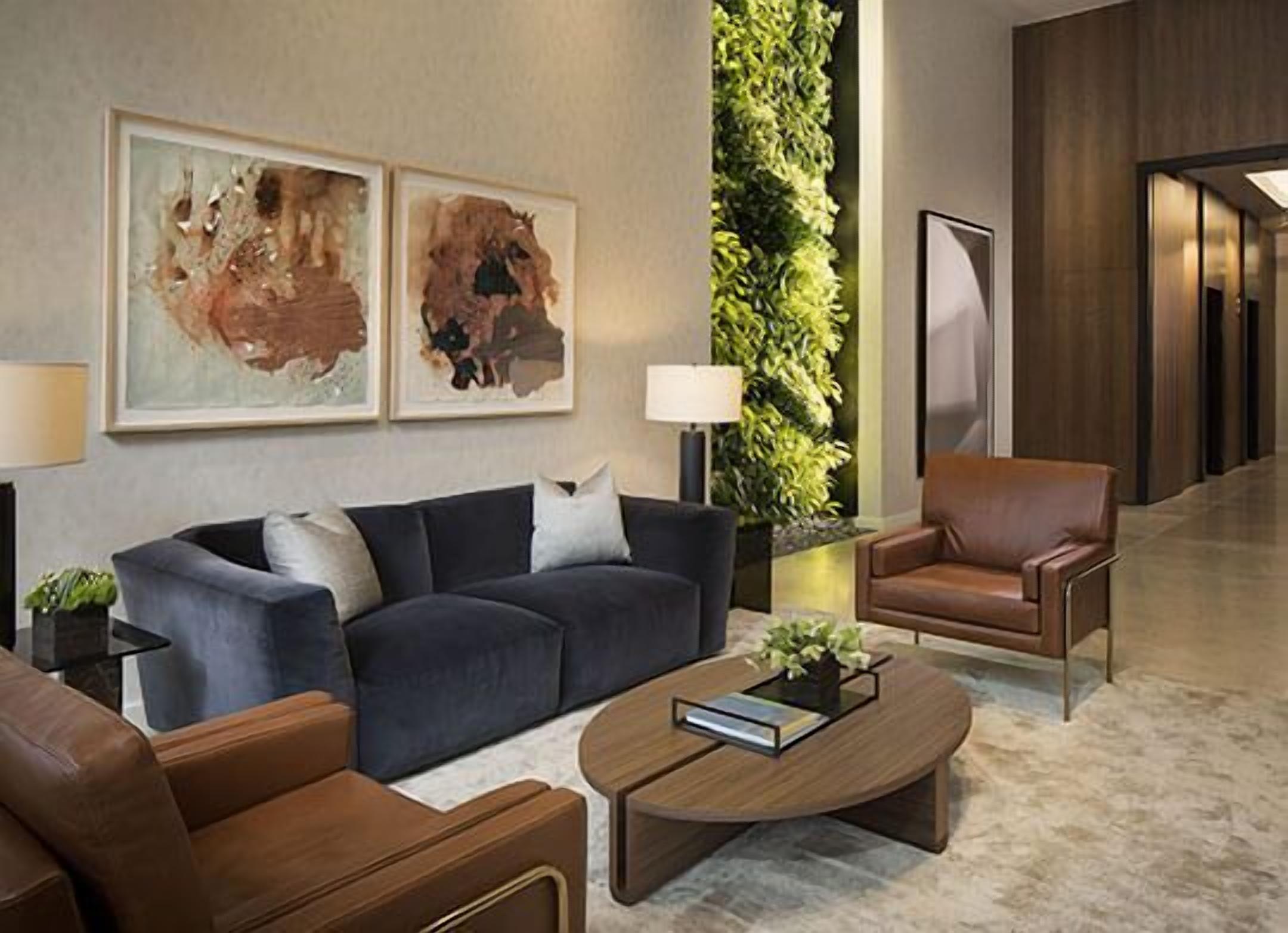 Eine moderne Lobby mit einem dunkelblauen Sofa, einem braunen Ledersessel, einem Holztisch und abstrakter Kunst an der Wand.