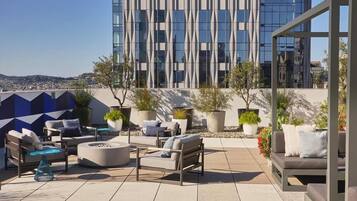A rooftop terrace with outdoor seating, potted plants, and a view of a modern building.