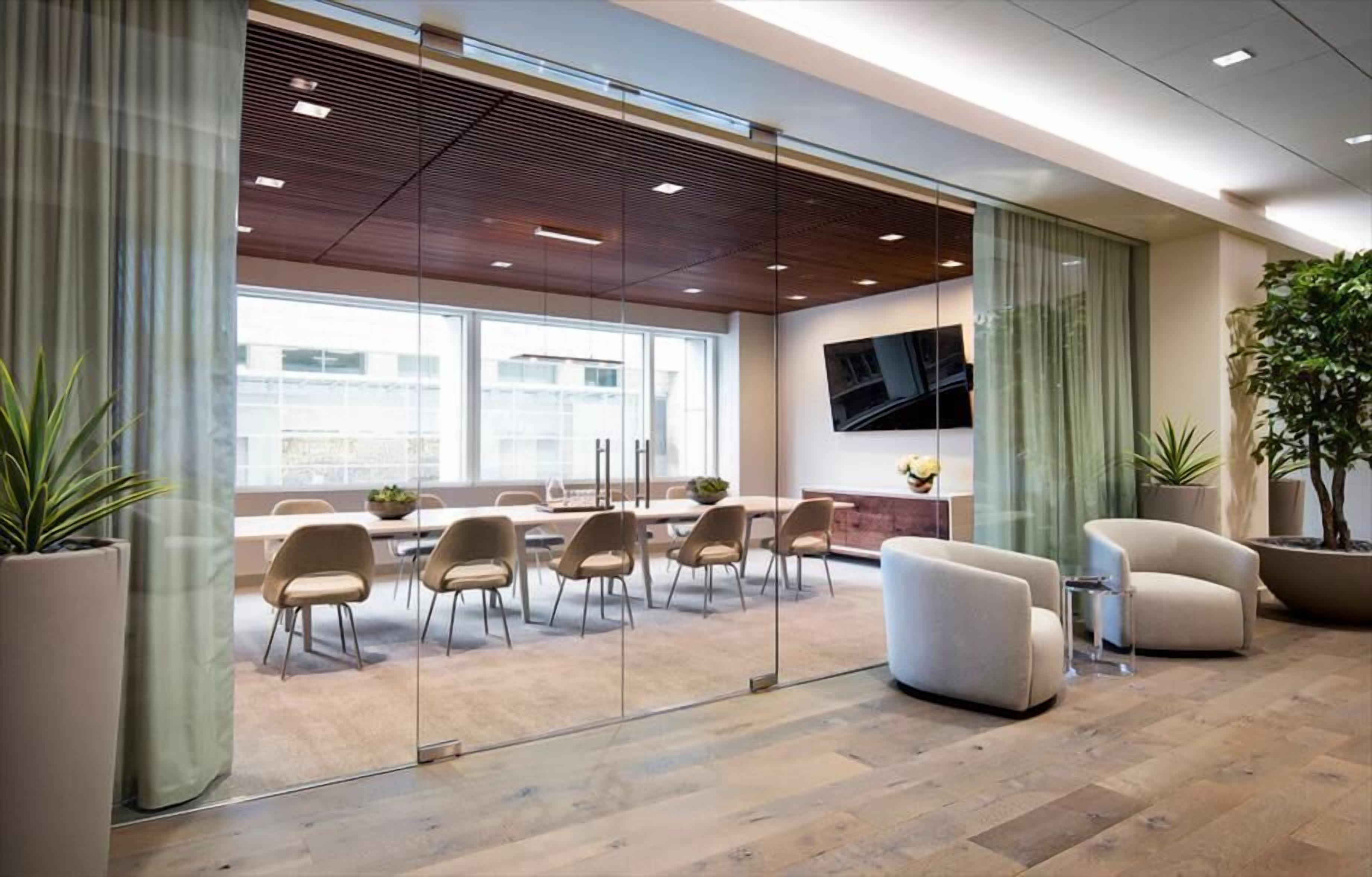 A modern conference room with glass walls, a large table, and several chairs.