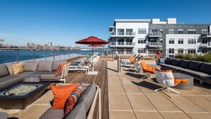A rooftop terrace with outdoor seating, a fire pit, and a view of the city skyline and water. - Boston Pier 1 BR | Close to Airport | Workspaces (East Boston)