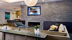 A modern living room with a stone wall, a fireplace, a large TV, and a glass coffee table. - Boston Pier 1 BR | Close to Airport | Workspaces (East Boston)