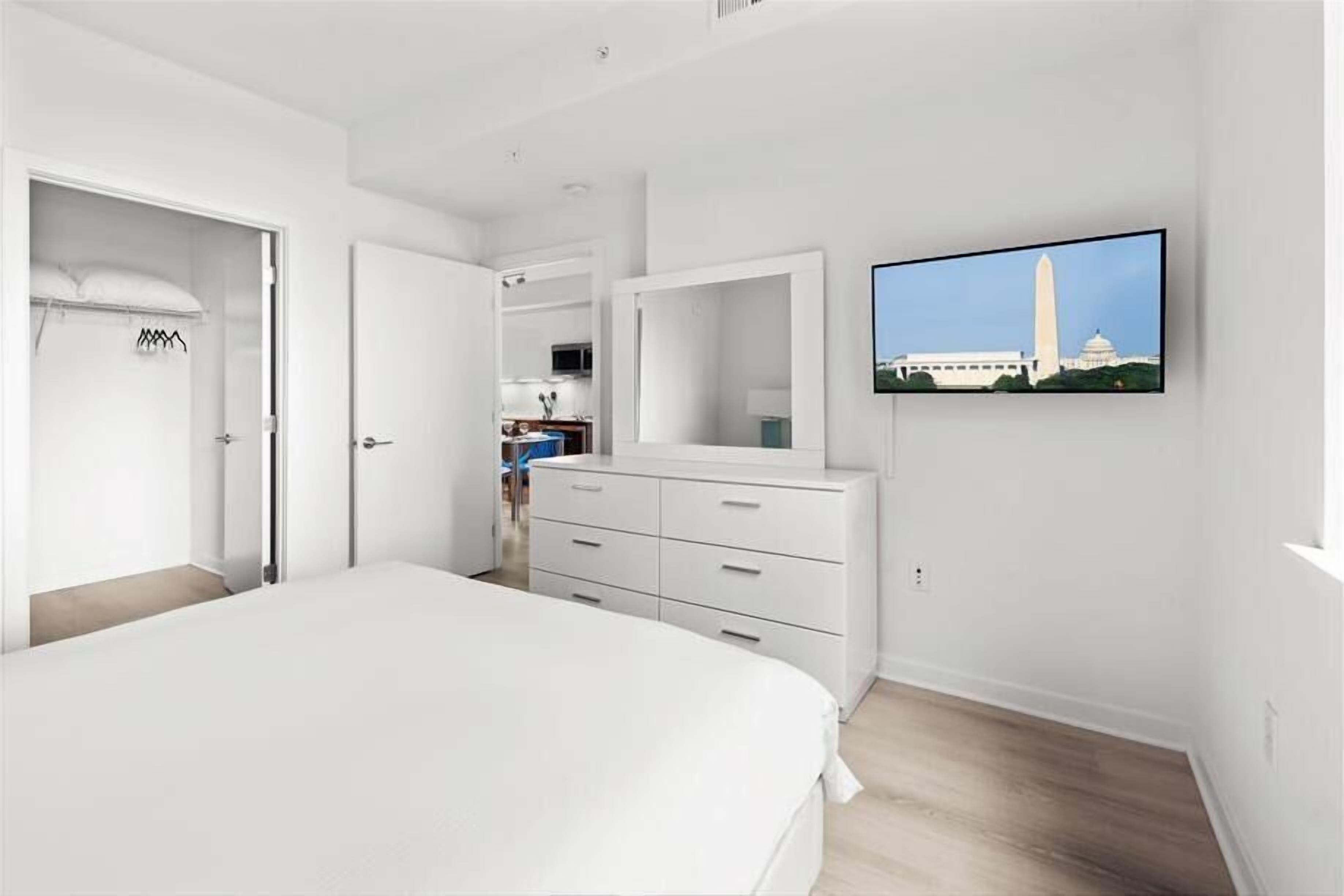 Une chambre avec un grand lit, une commode blanche, un téléviseur fixé au mur et une vue sur le Washington Monument.