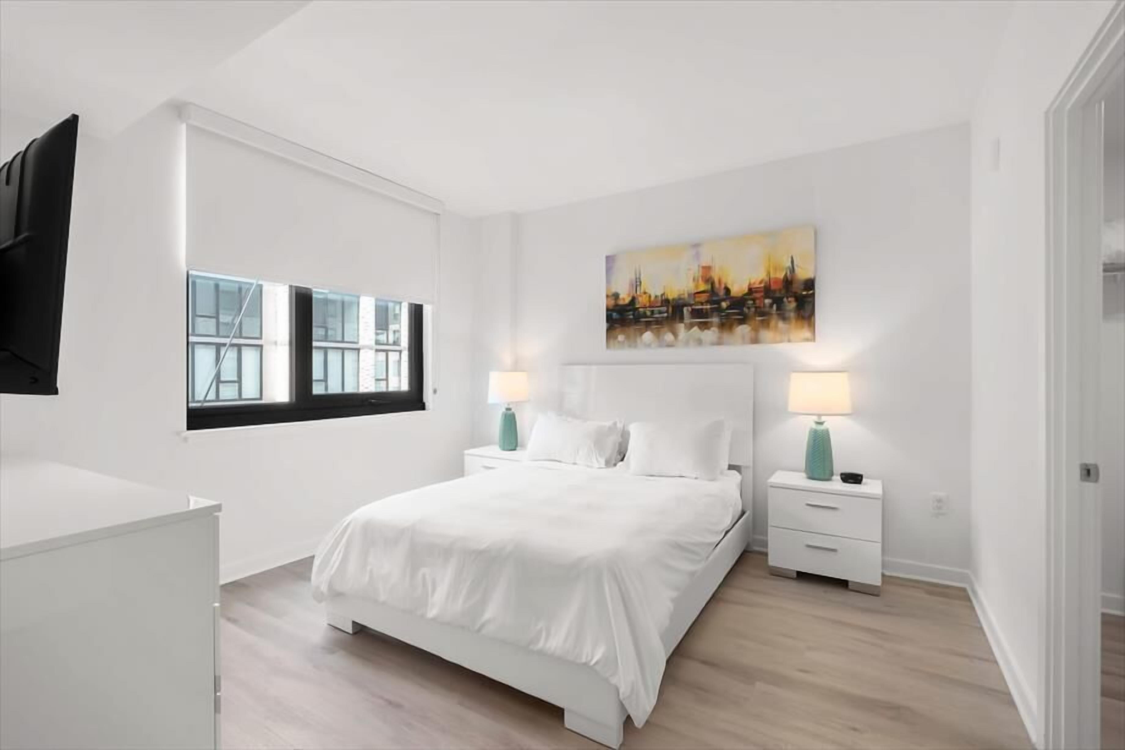A modern bedroom with a large bed, white nightstands, and a cityscape painting on the wall.