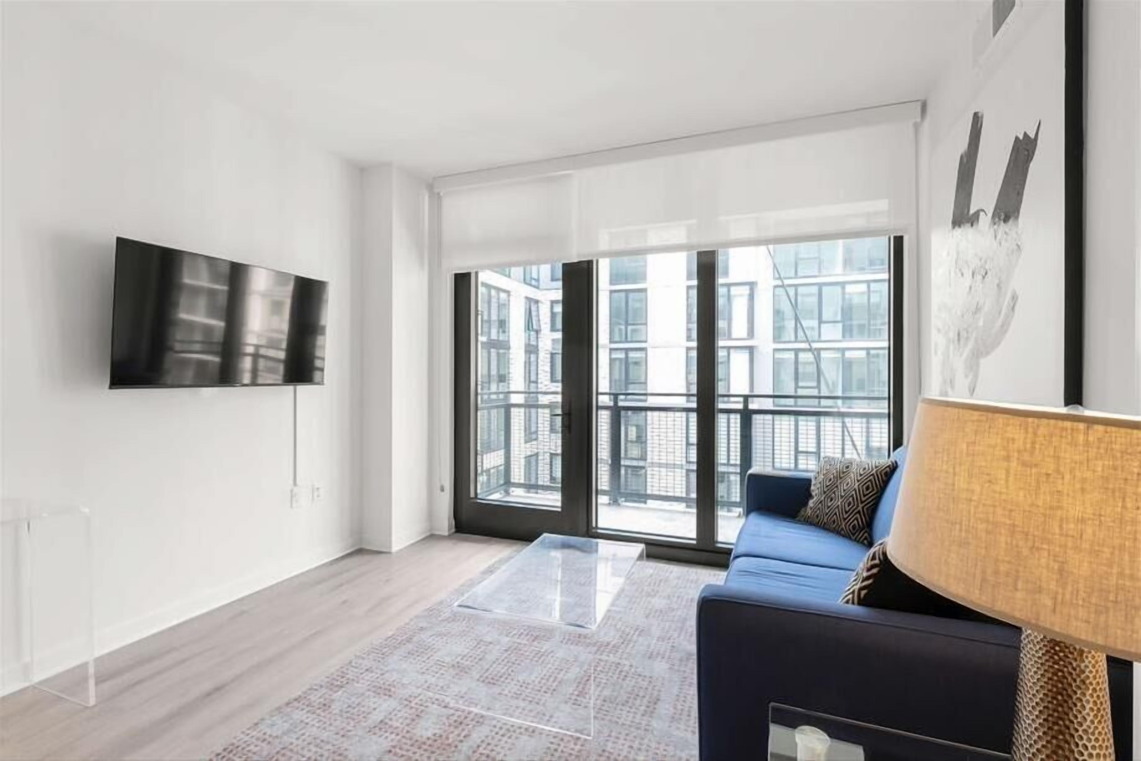 A modern living room with a large window, a flat-screen TV, a sofa, and a lamp.